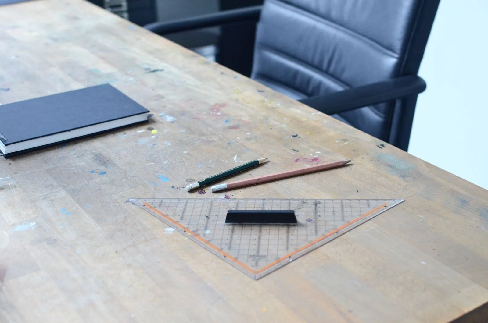 From above of notebook with pencils and ruler placed on shabby wooden table with colorful paints spots in workshop